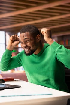 Joyful cheerful african american man at home celebrating, showing positive emotions. Delighted BIPOC person thrilled by achievement, cheering and gesticulating in apartment
