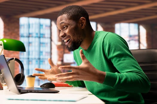 Joyous man at home office desk facing laptop screen, overjoyed by job achievement. Ecstatic remote employee reacting to positive result at work, looking at notebook screen