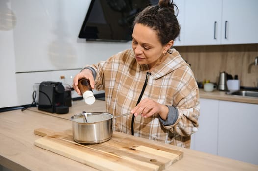 A woman is seen adding ingredients to a saucepan while cooking in a stylish kitchen.