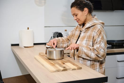 A cheerful woman enjoying cooking in her modern kitchen, preparing a delicious homemade meal on a wooden counter. The scene captures a relaxing and warm domestic atmosphere.