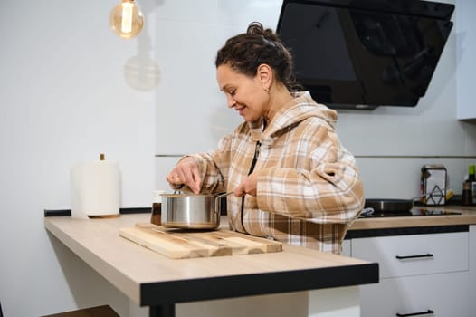 A young woman is enjoying cooking a meal in her bright and cozy kitchen, showcasing her culinary skills, surrounded by modern appliances and a warm ambiance.