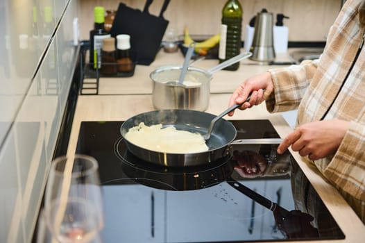 A person cooks crepes on a stove in a modern kitchen, with utensils and ingredients nearby. The setting suggests a cozy and inviting home environment, highlighting culinary activities.