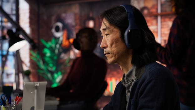 AI startup office chief technology officer listening music while coding application. Senior programmer wearing headphones while working in artificial intelligence software development agency, camera B