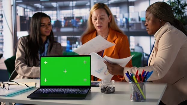 Multiethnic businesswomen working next to isolated green screen, solving daily tasks for a project to achieve enterprise objectives and work on global development. Corporate feminism. Camera B.