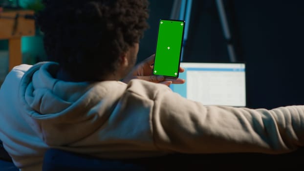 Confident tech user looking at isolated mockup display in his living room, relaxing with his remote job on the couch. African american happy adult browses the internet. Camera A.
