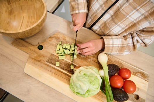 A person chops fresh vegetables, including cucumbers and lettuce, for a nutritious homemade salad. The setup includes kitchen tools, showcasing healthy food preparation in a cozy and inviting setting.