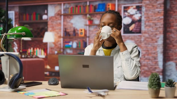 Woman enjoying leisure time at home, drinking coffee, texting friends on laptop. Cheerful person talking with mates on social network online website, using notebook, camera B