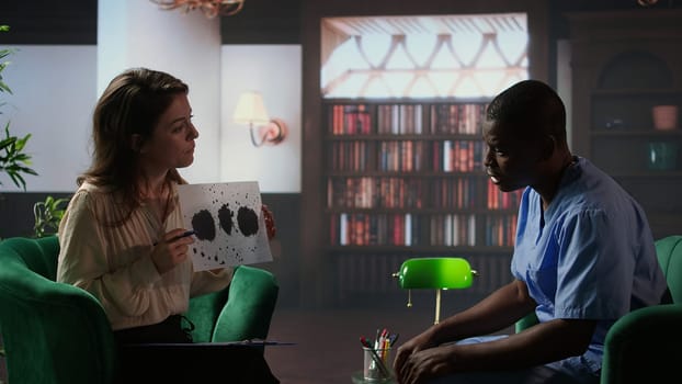 Counselor presents a Rorschach test to a medical assistant in uniform, looking for answers with psychoanalysis illustration. Nurse suffering from PTSD and trauma, interpretation therapy. Camera A.
