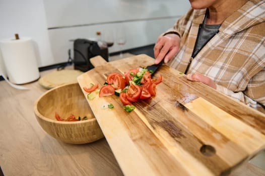 A close-up view of a woman preparing a fresh tomato salad on a wooden cutting board in a modern kitchen, embodying the theme of healthy lifestyle and home cooking.