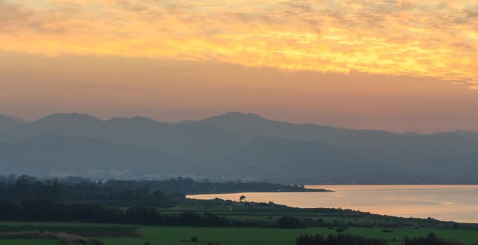 Golden hues illuminate the horizon as night approaches, casting a serene glow over water and landscape.