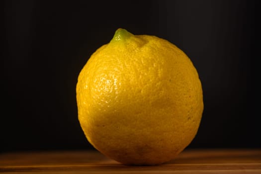 A vibrant lemon stands on a rustic wooden surface, illuminated by soft light that accentuates its fresh texture.