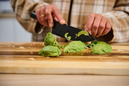 A close-up of hands slicing avocados on a wooden cutting board in a kitchen setting. The scene showcases fresh ingredients being prepared for a healthy meal, emphasizing fresh produce and culinary creativity.