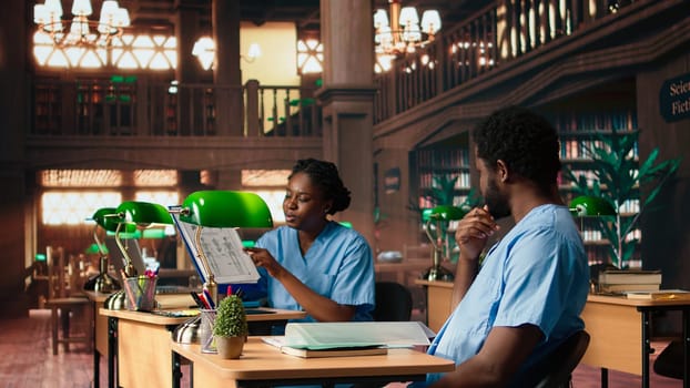 African american nurses in training review medical school papers and class notes, learning together and preparing for tests in the campus library. Healthcare practice for a medical career. Camera A.