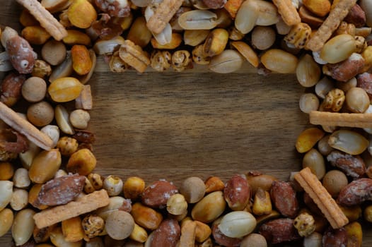 A vibrant array of nuts and savory snacks arranged beautifully around a wooden surface, perfect for sharing or as a delightful centerpiece during gatherings.