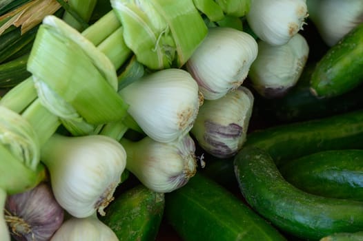 Bunches of crisp green onions and dark green cucumbers are arranged in a vibrant display, highlighting the freshness of the produce at a lively market. Customers enjoy browsing the colorful offerings.