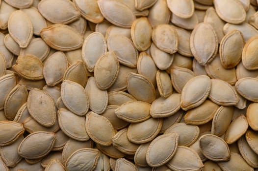 A multitude of pale pumpkin seeds lies scattered across a rustic wooden surface, reflecting the rich colors of autumn. The warm essence of seasonal gatherings fills the air.