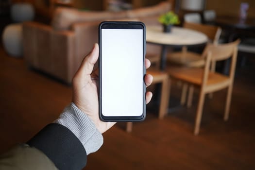 A person holds a blank smartphone in a stylish cafe interior.
