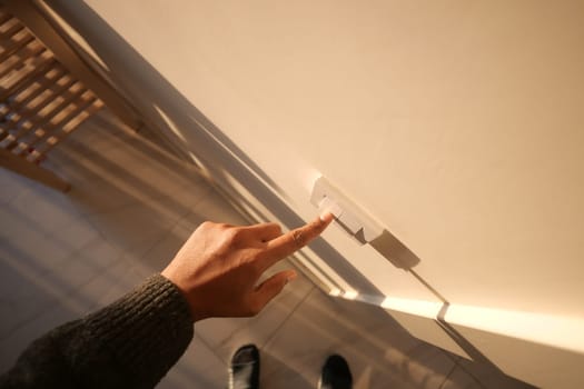 A hand reaches to switch on the light in a well-lit room.