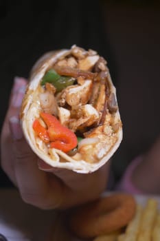 A hand holds a flavorful chicken wrap filled with colorful vegetables.