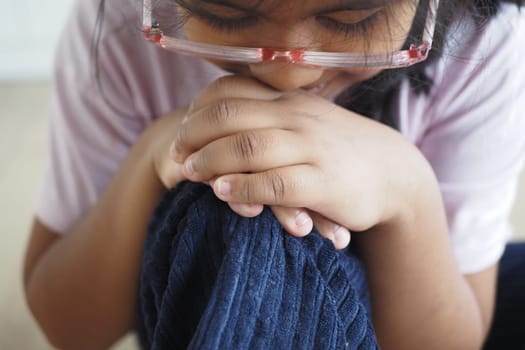 A young child sits quietly, hands clasped on knees, deep in thought.