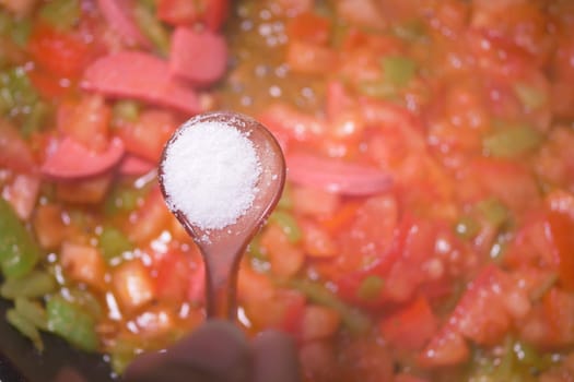 A hand adds salt to a colorful mix of vegetables on the stovetop.