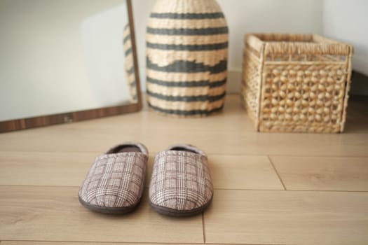 Warm slippers placed on wooden flooring next to woven storage baskets.