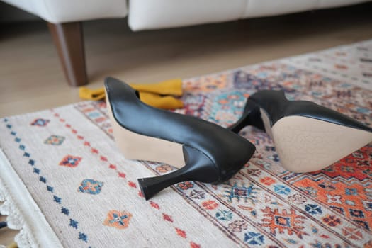 Two black high heels resting on a decorative rug in a cozy setting.