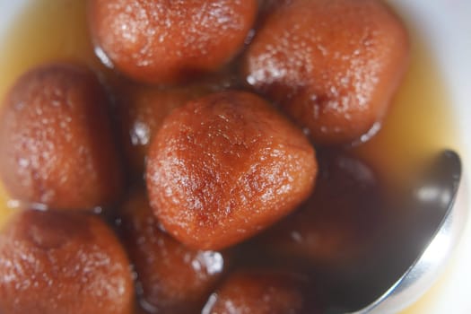 Delicious round dessert balls are soaked in sweet syrup in a bowl.