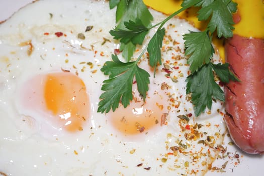 Two sunny-side-up eggs served with sausage and fresh herbs garnishing.