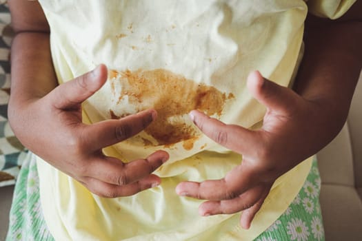 A child sits with hands on stomach, showing a stained yellow shirt.