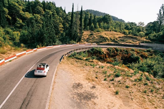 White car with a convertible top is driving along a road in the mountains. Drone. High quality photo