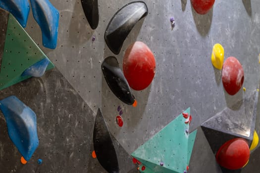 Colorful climbing holds on gray gym wall, showcasing a full frame of an artificial rock climbing wall with various handles for climbing in closeup