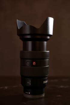 Replacement lens Sony FE 24-70mm for a digital camera with a cap stands on a black table. High quality photo