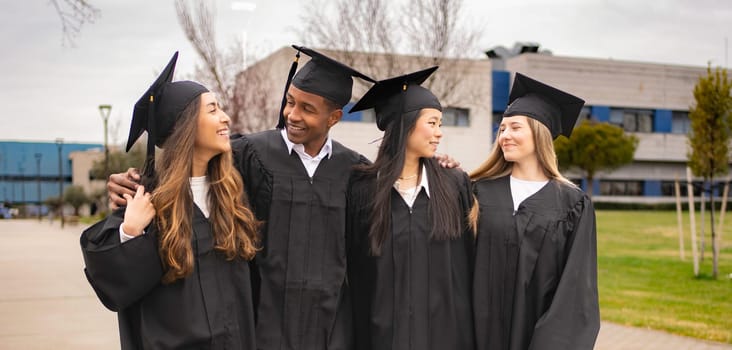 Happy multi-ethnic graduating students wearing gowns and caps are celebrating graduation