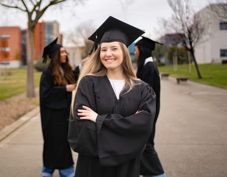 Young graduate student smiling with arms crossed on campus with other students in background