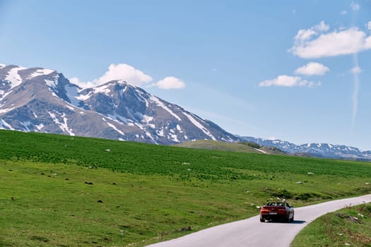 Red convertible is driving along a road in a green mountain valley. Back view. High quality photo