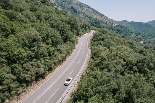 White convertible drives along a deserted highway in the highlands. Drone. High quality photo