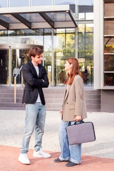business man and woman standing outside of an office building talking to each other, they are wearing casual clothes