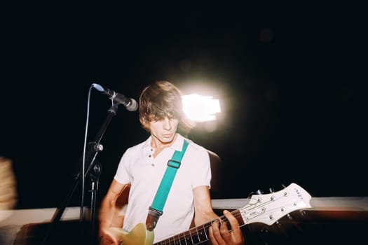Guitarist playing guitar into a microphone on stage at night near a spotlight. High quality photo