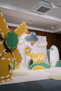 Actress with a jug stands on stage watering wheat decorations in a kindergarten. High quality photo