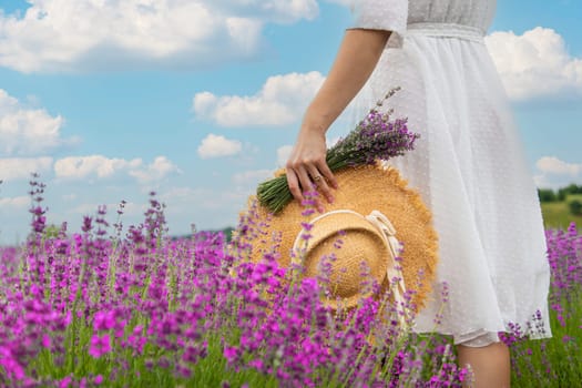 Woman holding lavender bouquet and hat in hands in lavender field.