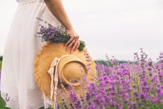 Woman holding lavender bouquet and hat in hands in lavender field.