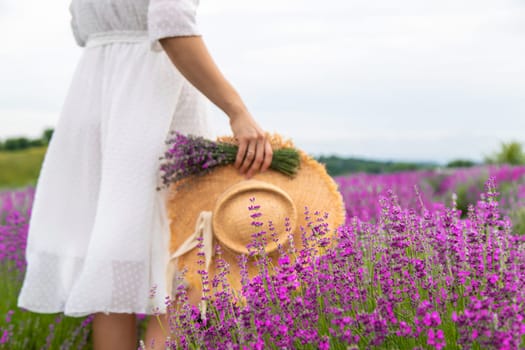 Woman holding lavender bouquet and hat in hands in lavender field.