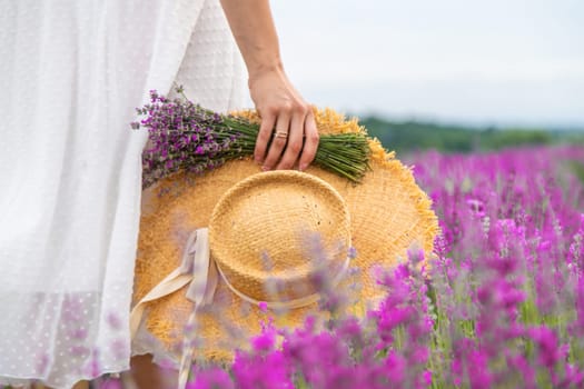 Woman holding lavender bouquet and hat in hands in lavender field.