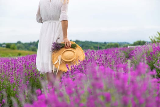 Woman holding lavender bouquet and hat in hands in lavender field.