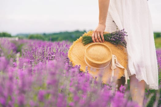 Woman holding lavender bouquet and hat in hands in lavender field.