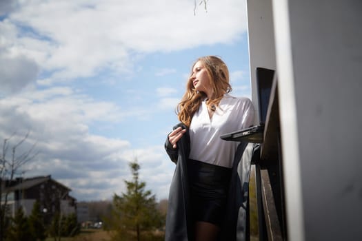 Woman stands outside on a sunny day, casually holding a laptop while enjoying the pleasant weather.