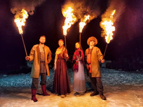 Actors in ethnic costumes perform a captivating fire show on a frost-covered landscape, embracing Viking culture on a winter night.