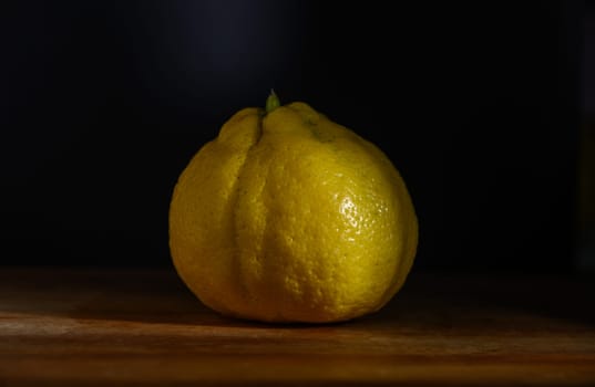 A beautifully shaped yellow lemon sits on a wooden table, illuminated gently to accentuate its texture and color.