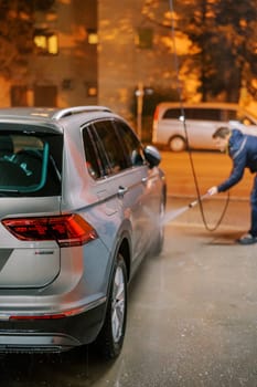 Washer at a car wash washes the wheels of the car with a hose. High quality photo